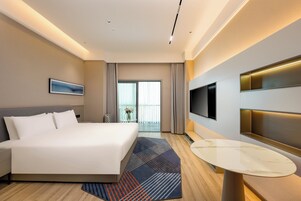 Una habitación de hotel con una cama grande, un televisor en la pared y un balcón con cortinas.