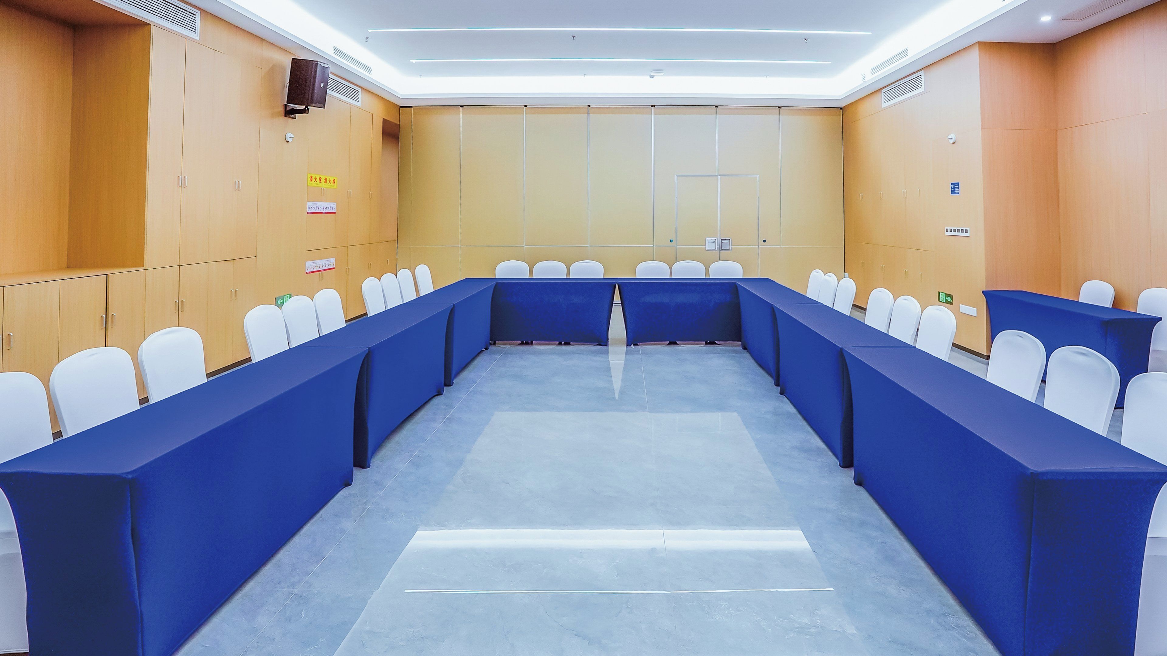 Un salón de conferencias con una larga mesa, sillas blancas y manteles azules.
