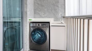 A compact laundry area with a front-loading washing machine, a small sink, and a glass door leading to a hallway.