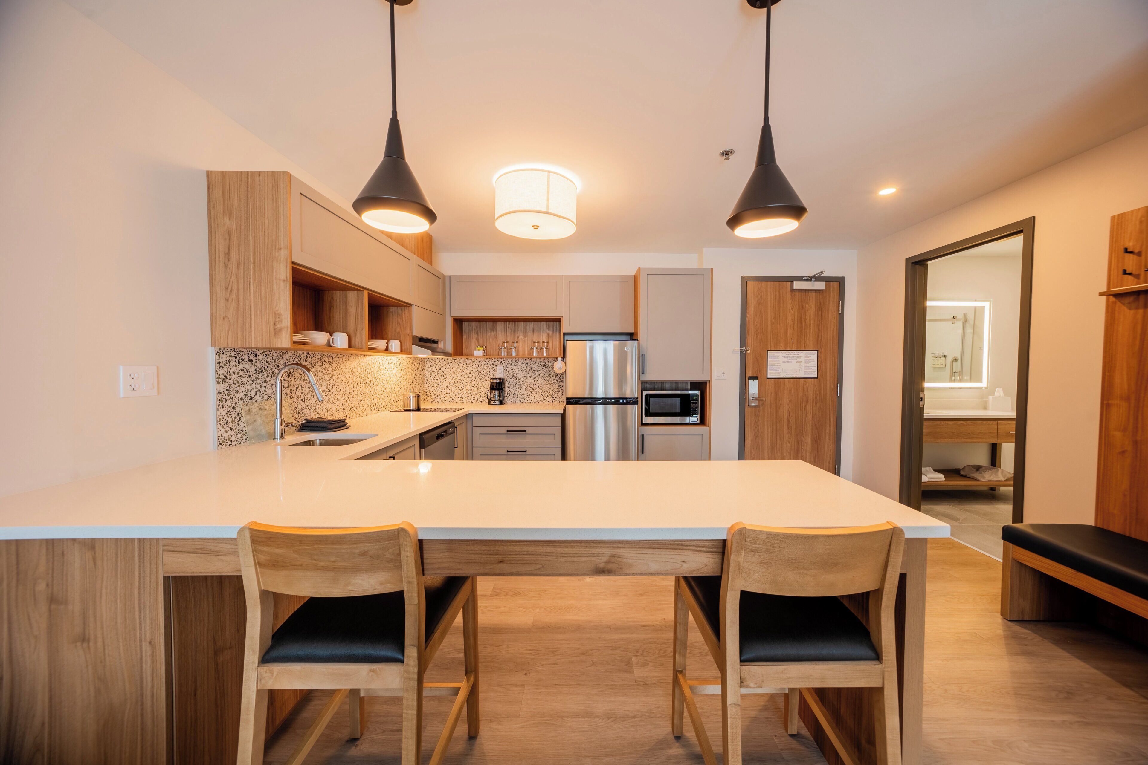A modern kitchen with a large island, wooden chairs, pendant lighting, and stainless steel appliances.