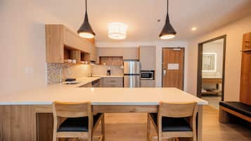 A modern kitchen with a large island, wooden chairs, pendant lighting, and stainless steel appliances.