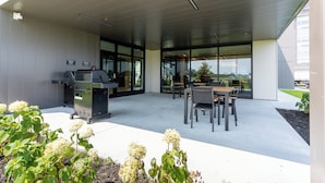 An outdoor patio with a grill, seating area, and large windows.