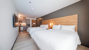 Une chambre d’hôtel moderne avec deux lits, une tête de lit en bois, un coin cuisine et un téléviseur à écran plat.