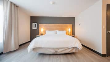 A hotel room with a large bed, two bedside lamps, a wooden headboard, a framed picture on the wall, and a door on the right.