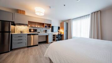 A modern hotel room with a kitchenette, a bed, a desk, and a television.