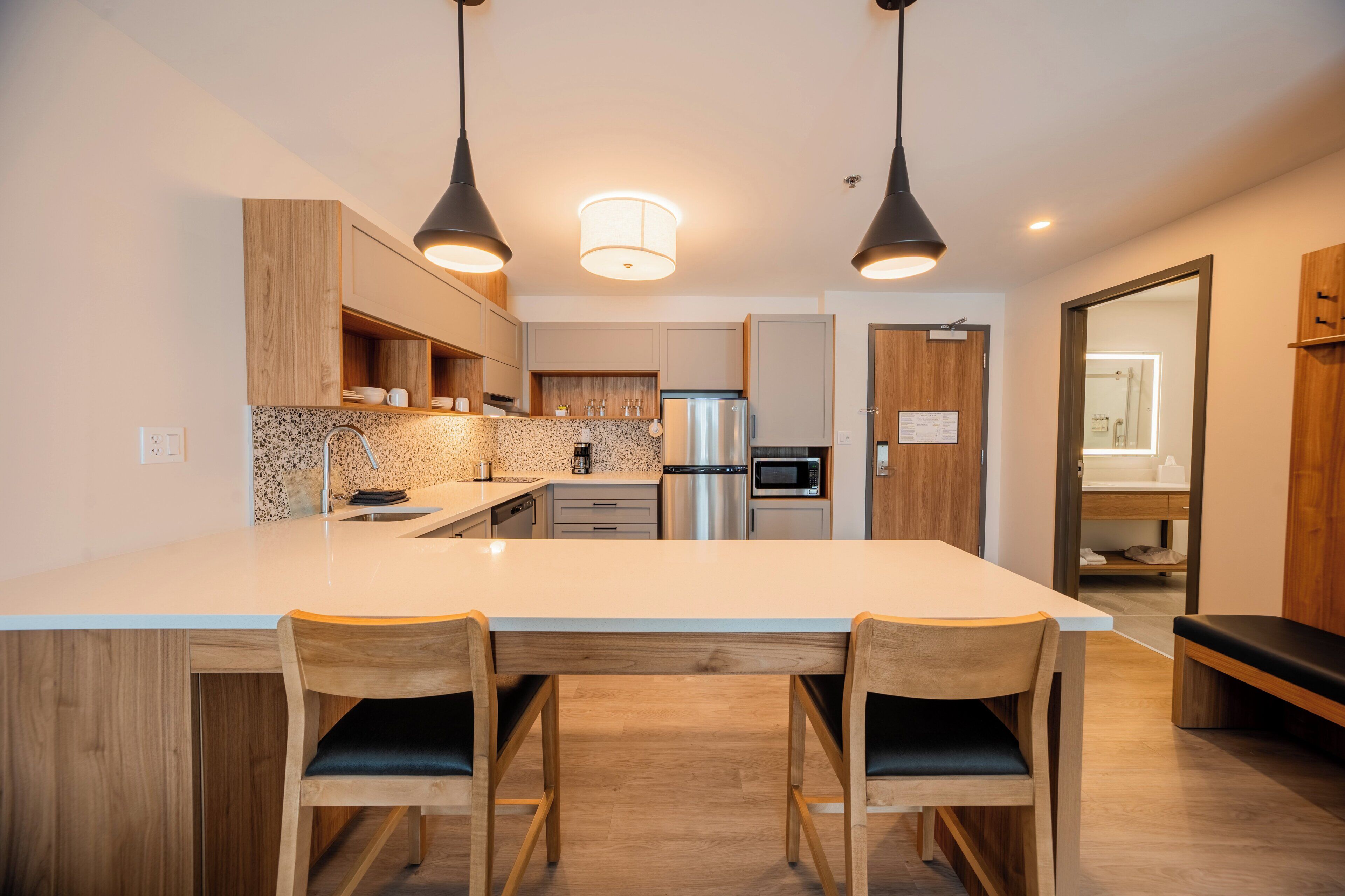 Une cuisine moderne dotée d’un îlot central, de meubles en bois, d’appareils électroménagers en acier inoxydable et de luminaires suspendus.