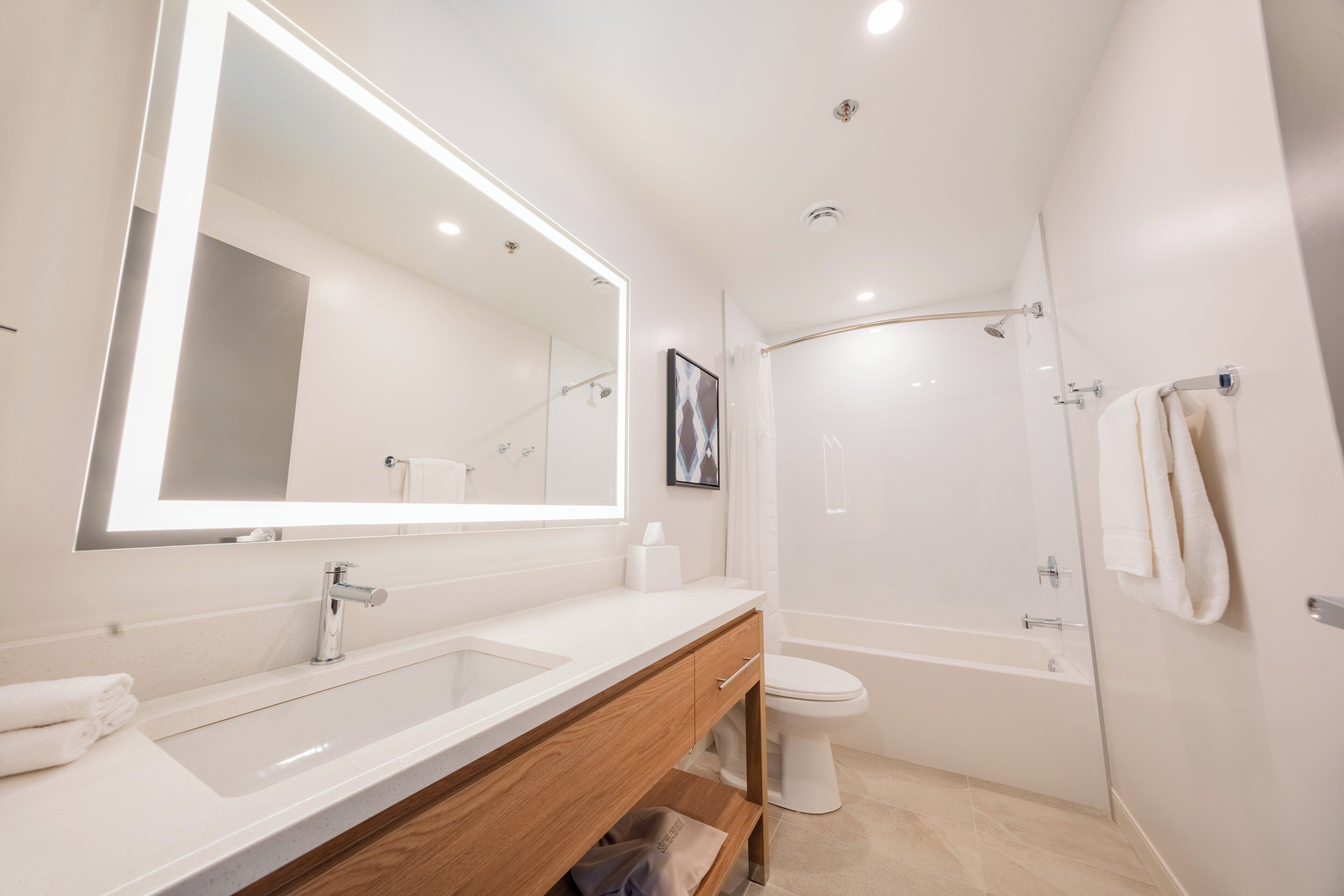 Un baño moderno con un espejo grande, un lavabo, un inodoro y una ducha.