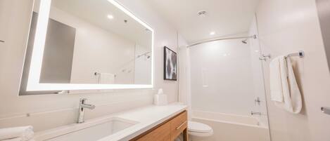 Un baño moderno con un espejo grande, un lavabo, un inodoro y una ducha.