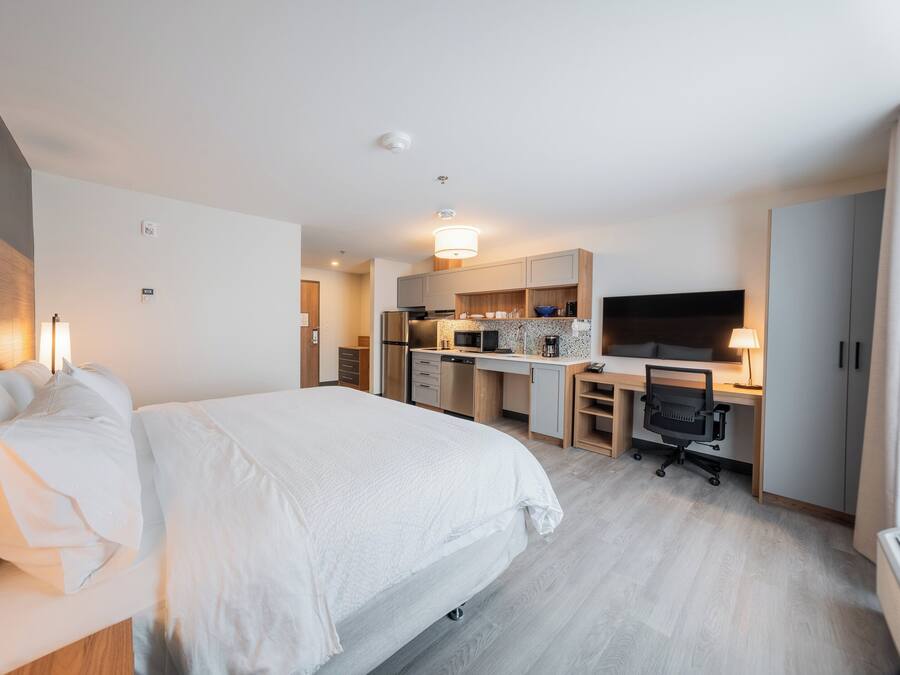 Habitación de hotel moderna con una cama grande, kitchenette, escritorio y televisor.