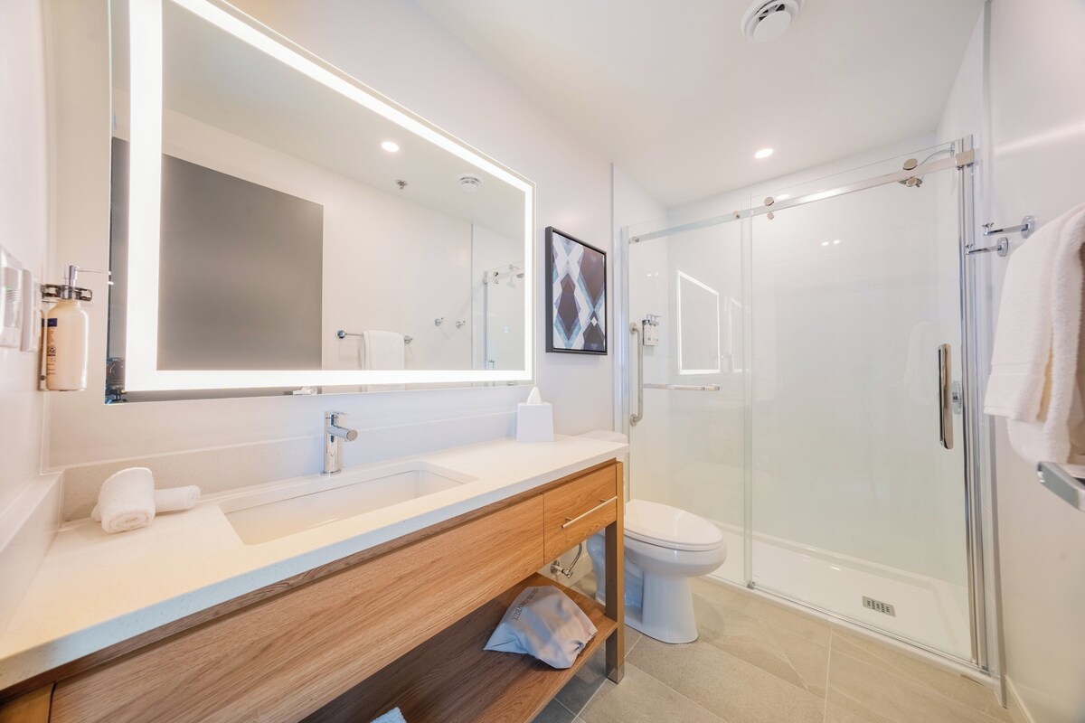 A modern bathroom with a large mirror, a sink, a toilet, and a glass-enclosed shower.