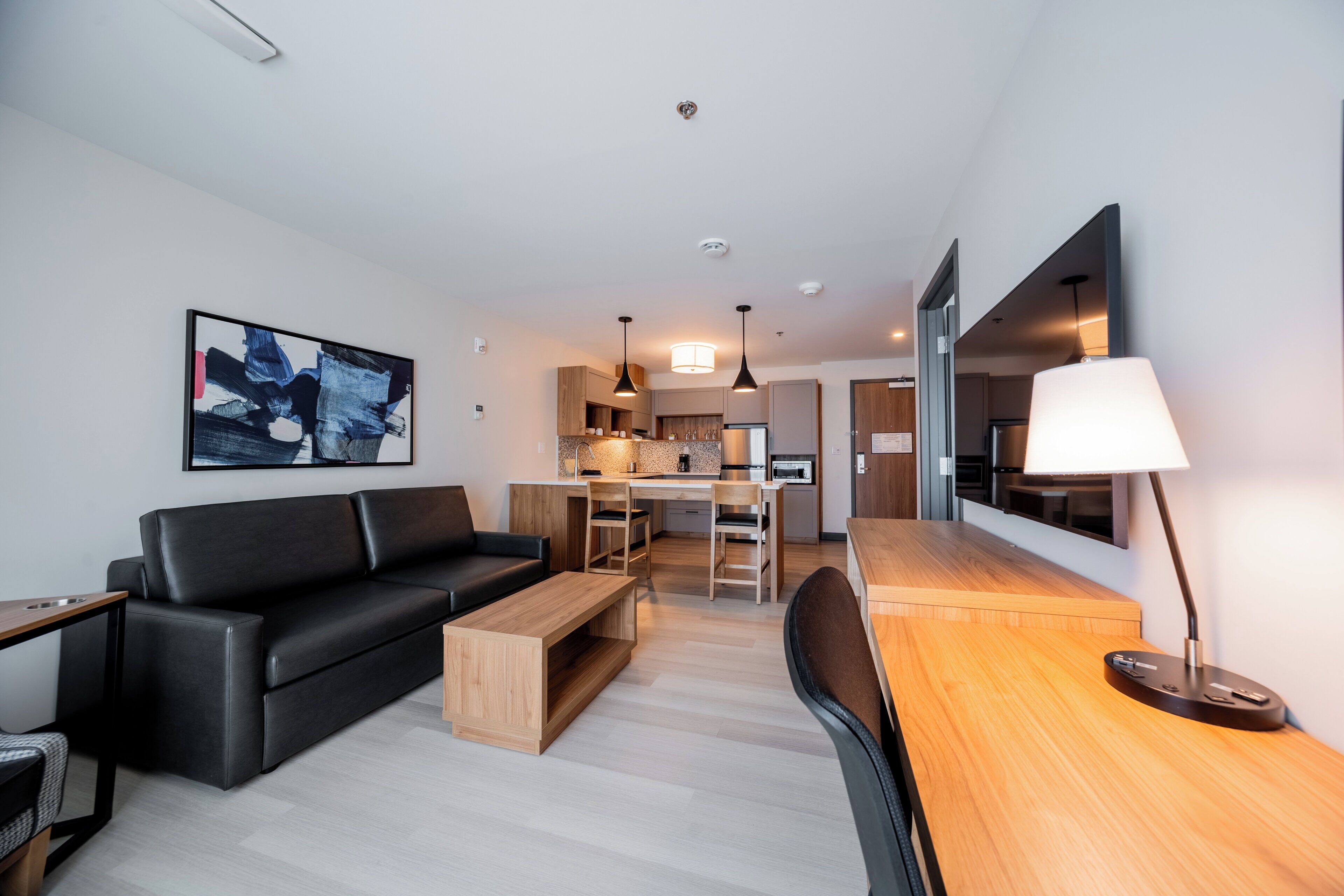 Una sala de estar moderna con un sofá negro, una mesa de centro de madera y un comedor con mesa y sillas de madera.