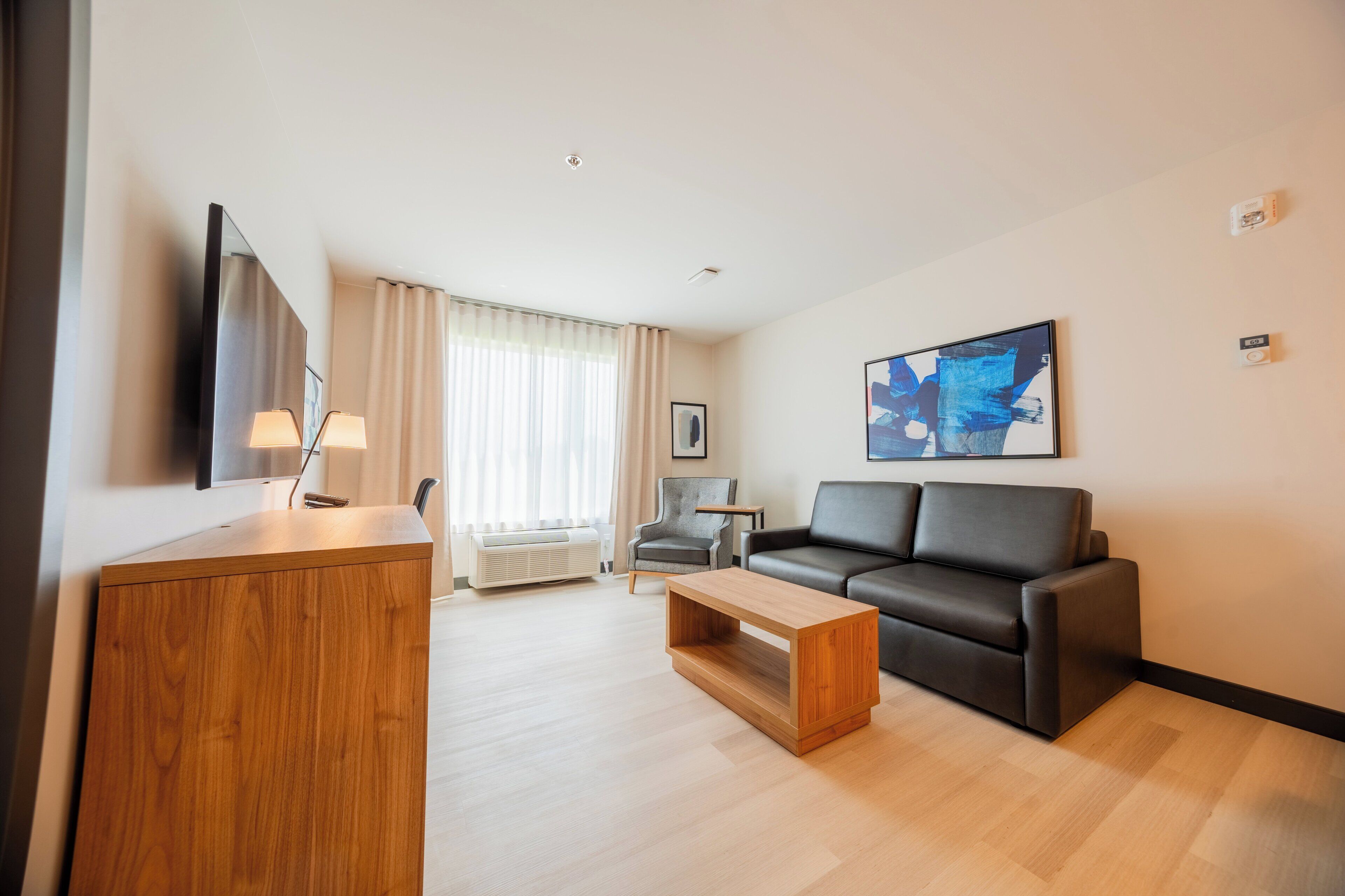Un salon moderne avec un meuble en bois, un canapé en cuir noir, une table basse en bois et un grand tableau abstrait accroché au mur.