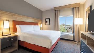 A hotel room with a bed, bedside tables, a desk, a television, and a window with curtains.