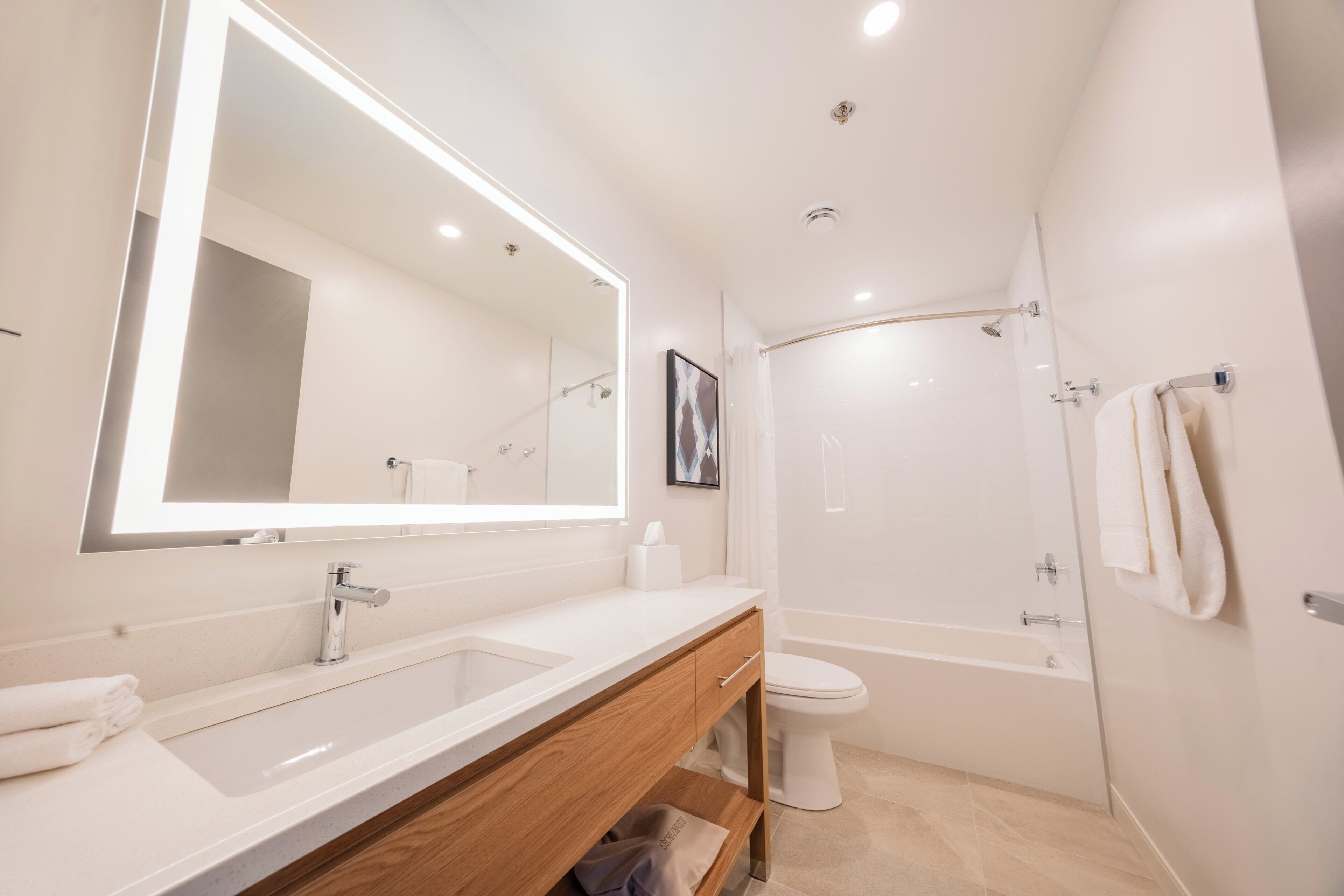 A modern bathroom with a large mirror, a sink, a toilet, and a shower.