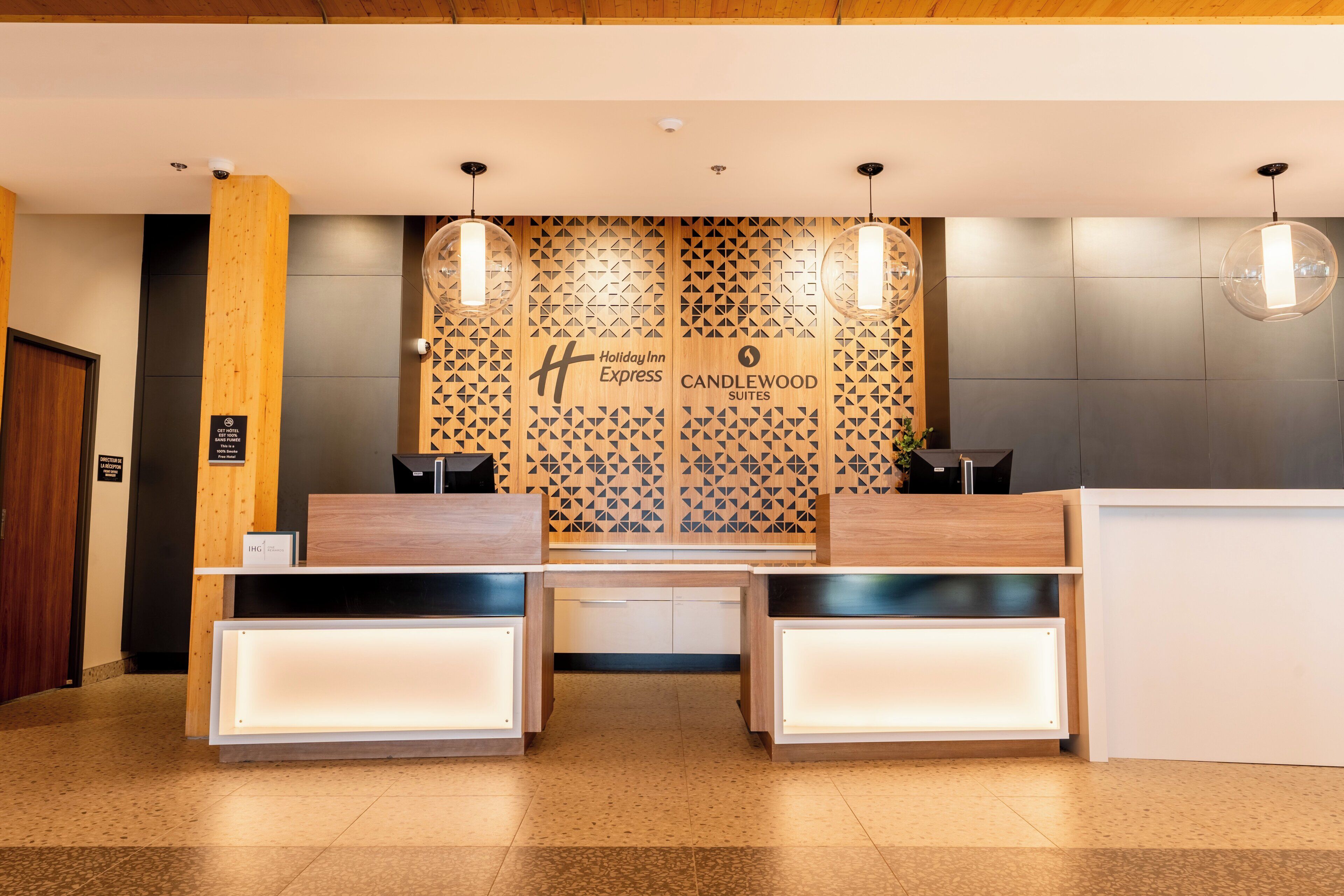 Un comptoir d’accueil, avec un mur à motifs géométriques en arrière-plan, où sont affichés les logos de Holiday Inn Express et de Candlewood Suites.