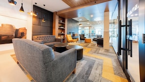 A modern lounge area with grey sofas, black ottomans, and wooden shelves.