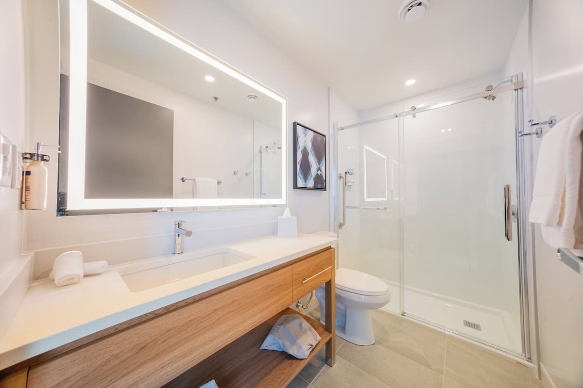Un baño moderno con un espejo grande, un lavamanos, un inodoro y una ducha con cerramiento de vidrio.