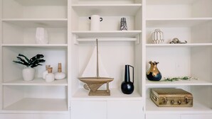 Une étagère blanche ornée de divers objets décoratifs, notamment une plante, un vase et une petite sculpture.
