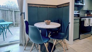 Un coin repas avec une table ronde et quatre chaises, un luminaire suspendu et une vue sur la cuisine.
