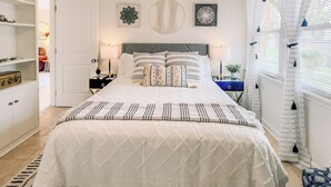 Une chambre à coucher avec un grand lit, une table de chevet, une commode et une fenêtre avec des rideaux.