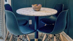 Une table ronde surmontée d’un plateau en marbre, entourée de quatre chaises bleu foncé à pieds en bois. Un bol en bois est posé sur la table.