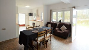 A dining area with a table set for four, a sofa, and a kitchen in the background. - Nature Retreat by the Lakes (Florennes)