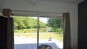 A bedroom with a large sliding glass door leading to an outdoor area with a lawn and a pond. - Nature Retreat by the Lakes (Florennes)