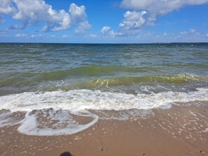 Une plage avec des vagues, un ciel dégagé et une terre lointaine à l’horizon.