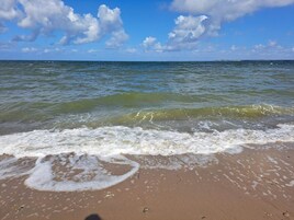Una playa con olas, cielo despejado y una tierra firme a lo lejos.