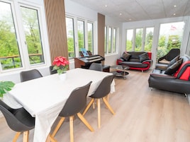 A modern living room with a piano, a dining table with chairs, and a sofa with red accents.