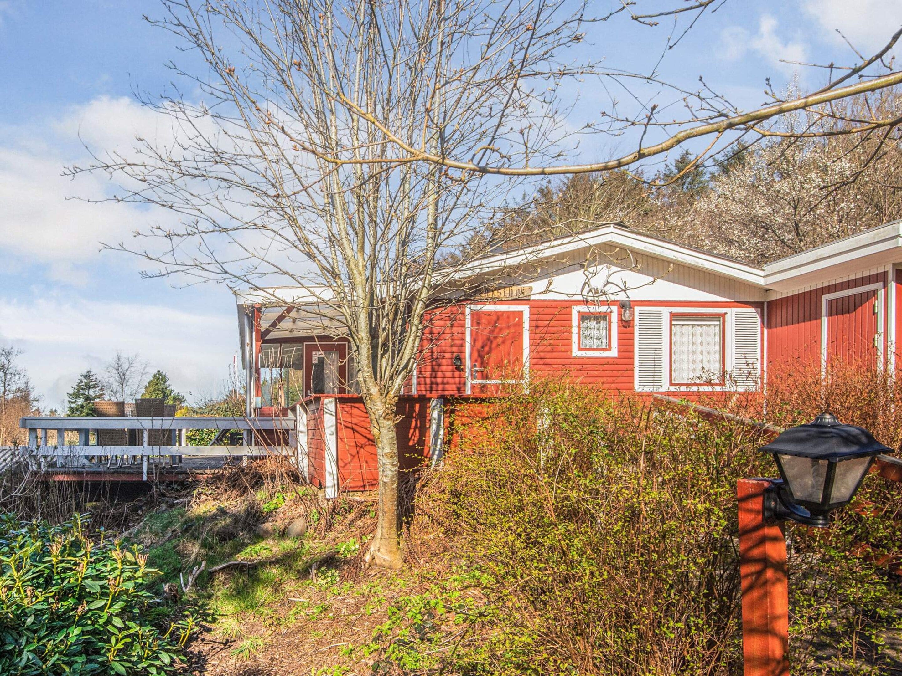 A red house with a white door, surrounded by greenery and a clear sky.