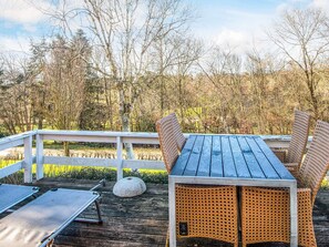 Une terrasse en bois, agrémentée d’une table et de chaises, entourée d ’une balustrade blanche, et offrant une vue sur une zone boisée.