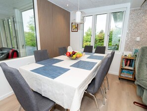 Un coin repas avec une table dressée pour quatre personnes, un panier de fruits et une bibliothèque remplie de livres.