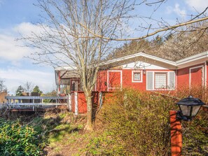 A red house with a white window and a door, surrounded by greenery and a clear sky.
