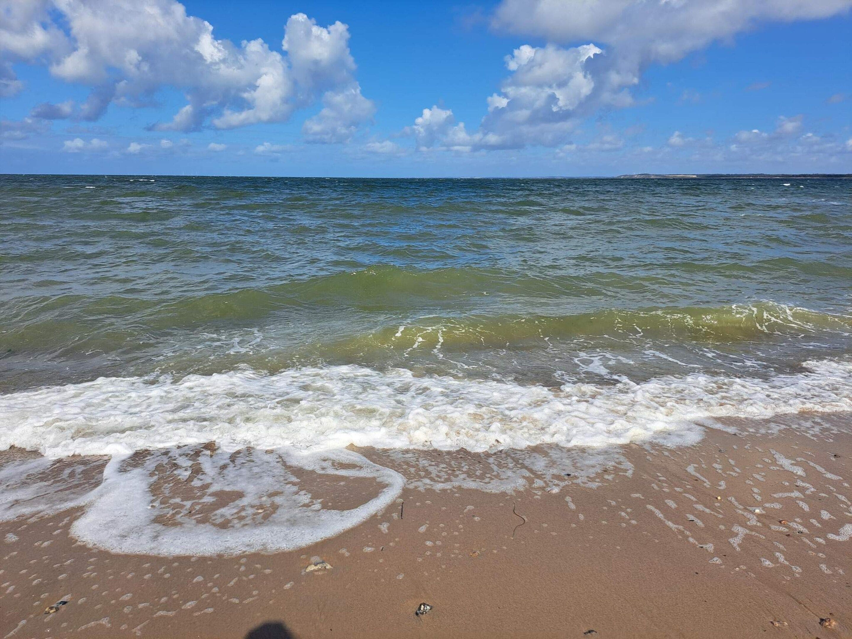 Une plage où les vagues viennent lécher le rivage sous un ciel partiellement nuageux.