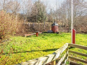 A wooden bench, a small red structure, and a wooden fence in a grassy area with trees in the background. - 6 Person Holiday Home in Struer (Struer)