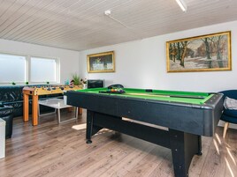 Una mesa de billar con fieltro verde, una mesa de fútbol de mesa y un sofá en una habitación con pisos de madera y paredes blancas.