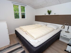 A bedroom with a bed, bedside table, lamp, and a window with a view of greenery.
