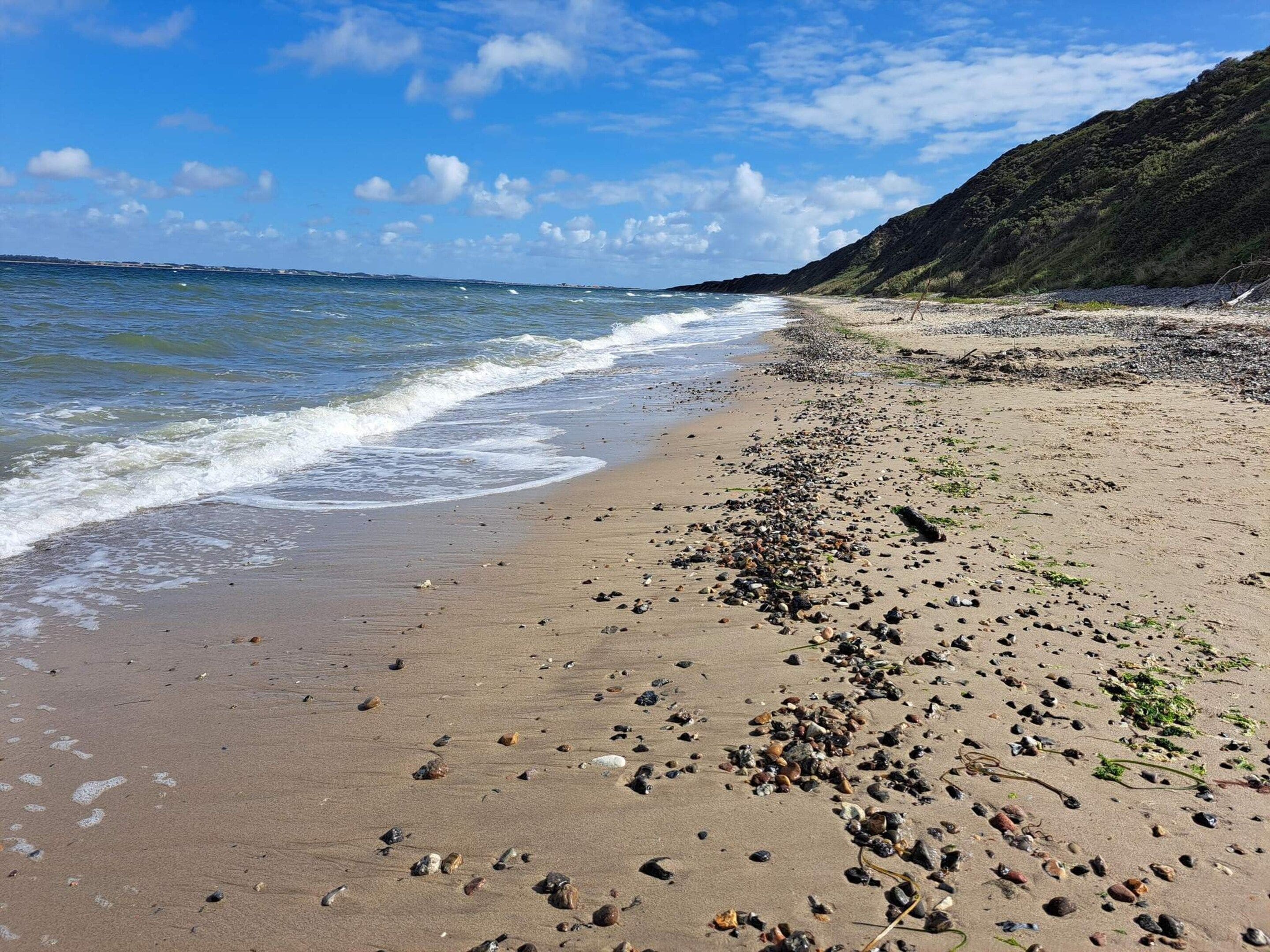 En strand med småsten och en klippig kustlinje.