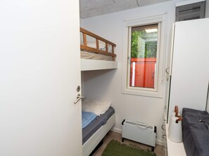 Una habitación pequeña y funcional con literas, un radiador, una ventana que da a zonas verdes y una puerta.
