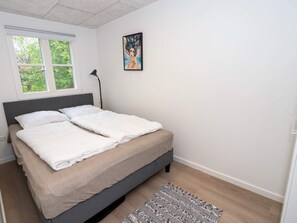 Un dormitorio con cama, ventana, lámpara de pie y un cuadro en la pared.