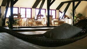 A room with a high ceiling, exposed wooden beams, a wicker sofa with a pillow, and a dining area with wicker chairs and a table. - Quellenhof Comfortable Holiday Residence (Retschow)