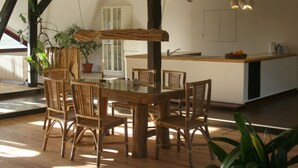 A dining area with a wooden table and chairs, a kitchen in the background, and potted plants. - Quellenhof Comfortable Holiday Residence (Retschow)