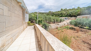 A balcony with a stone wall, a tiled floor, and a view of a rural landscape with trees and a vehicle. - Nice home in Zrnovo with house sea view (Zrnovo)
