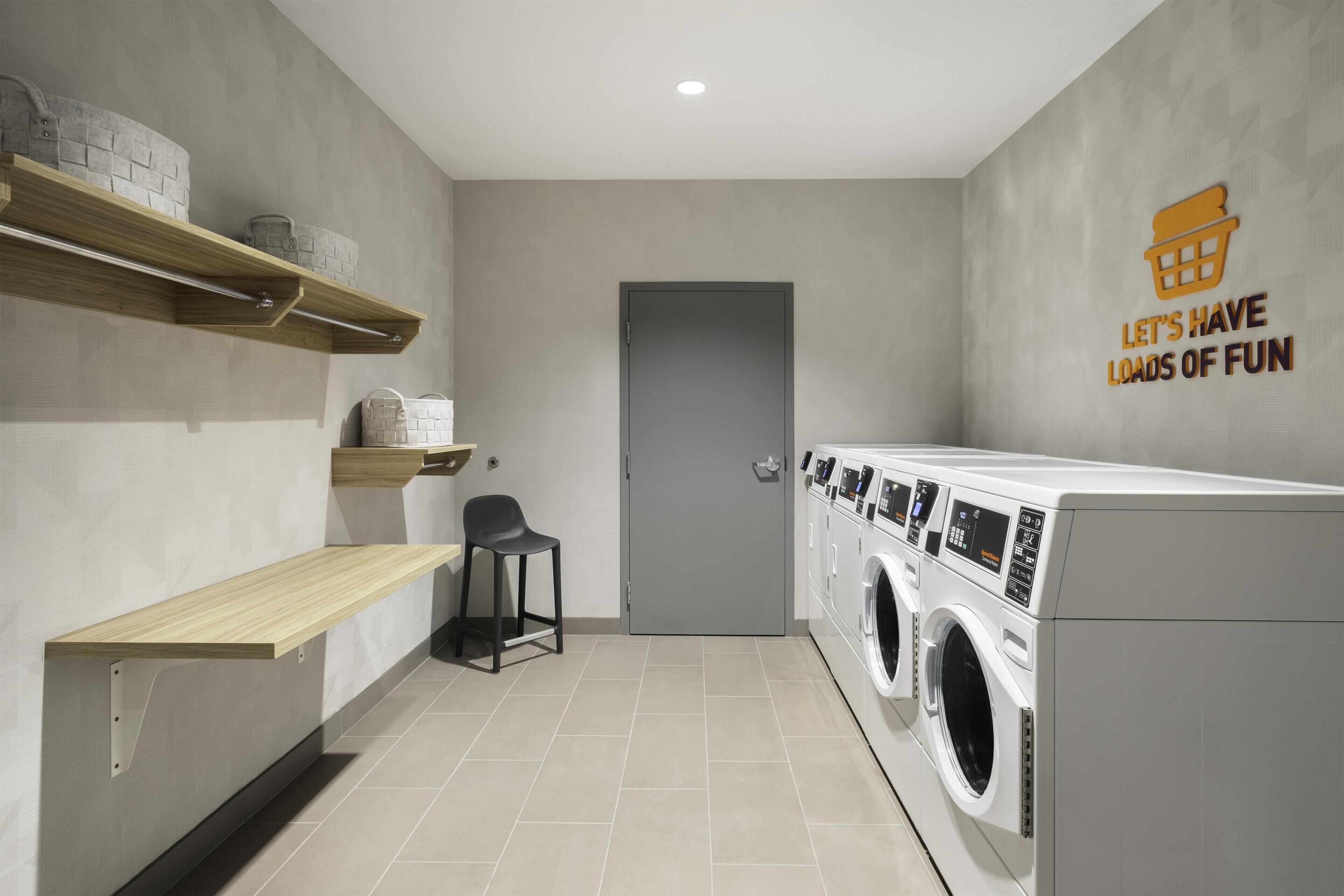 A laundry room with a washing machine, a chair, and a shelf with storage bins.