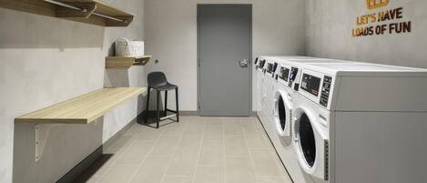 A laundry room with a washing machine, a chair, and a shelf with storage bins.