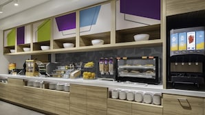 Un bar à petit-déjeuner moderne, équipé d’une machine à café, d’un présentoir de fruits et d’un distributeur de jus.