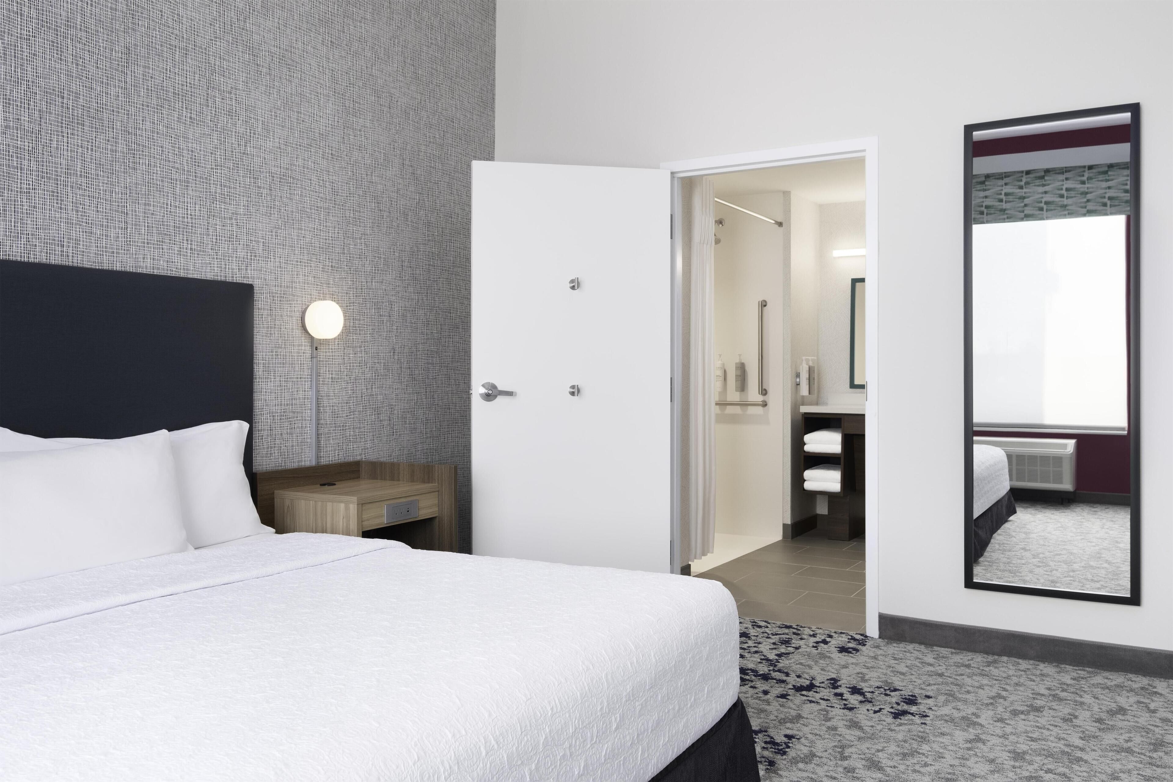Une chambre d’hôtel comprenant un lit, une table de chevet, un miroir et une porte donnant accès à une salle de bain.