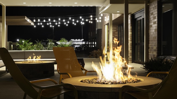 Un espace extérieur aménagé avec un foyer, des chaises et des guirlandes lumineuses.