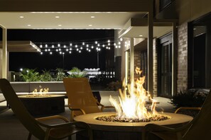 Un espace extérieur aménagé avec un foyer, des chaises et des guirlandes lumineuses.